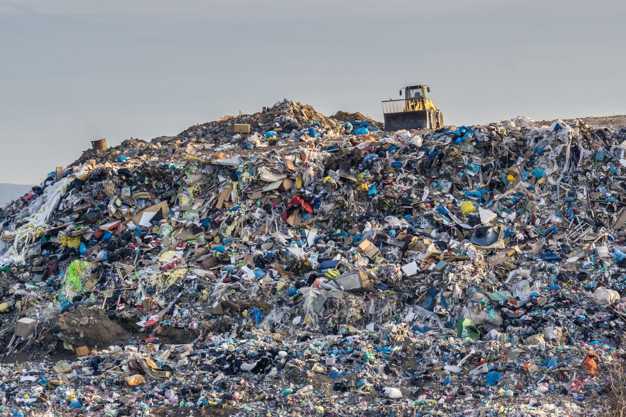 Un bulldozer travaille parmis des déchets et de débris mélangés sur la surface d'une grande décharge publique.